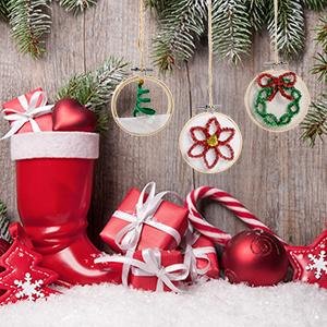 Three small wooden embroidery hoops decorated with Christmas designs, hanging amongst festive decorations and gifts.