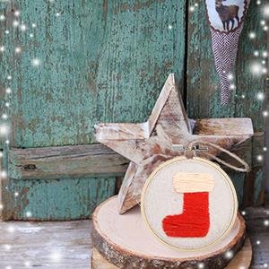 Embroidery hoop with red stocking design, displayed with a wooden star and rustic background.