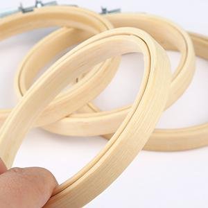 Close-up of several round wooden embroidery hoops with brass screws, held by a hand.