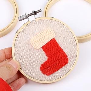 Hand holding a 3-inch round wooden embroidery hoop with a small red and cream stocking stitched onto the fabric inside.