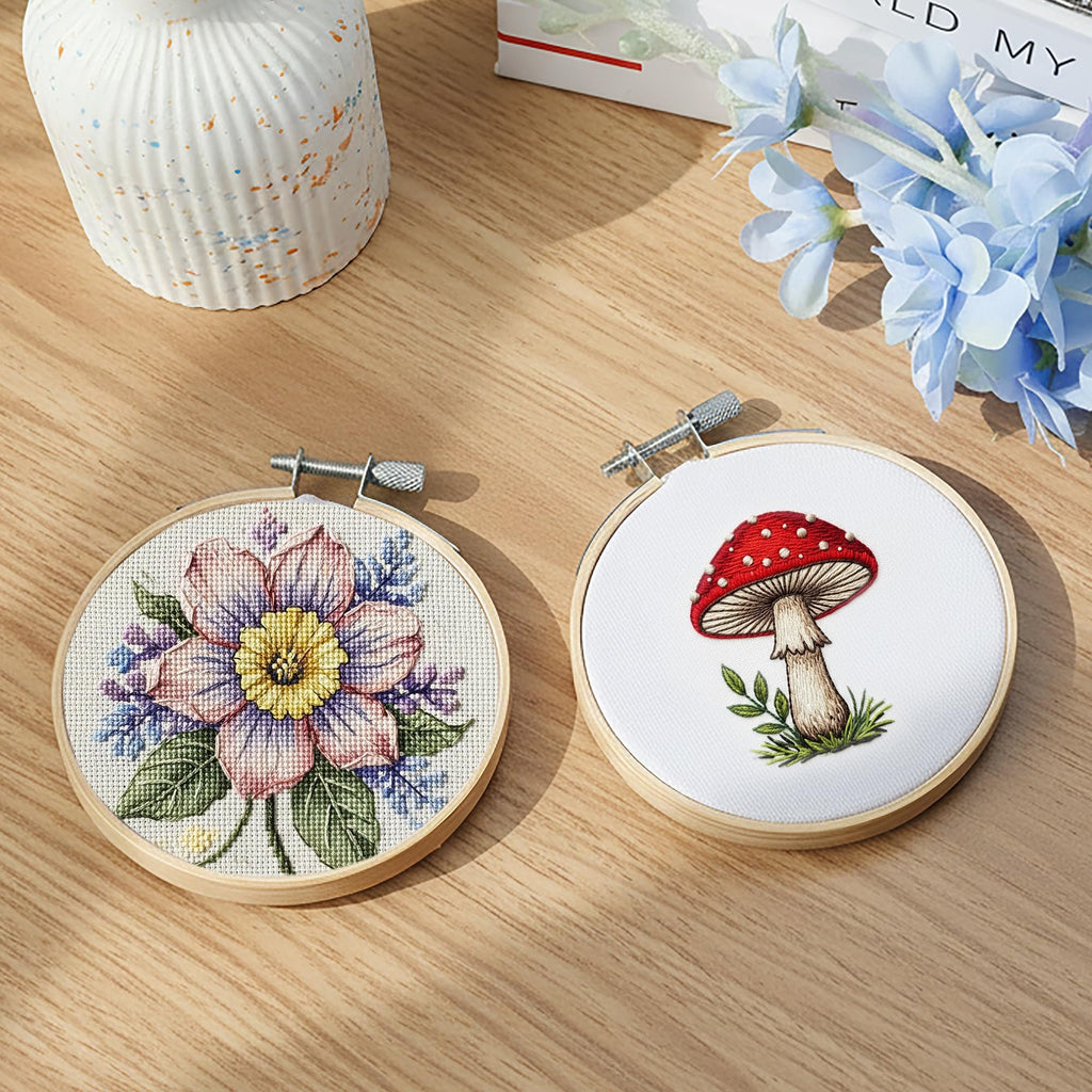 Two 3-inch round embroidery hoops, one with a floral cross-stitch design and the other with a mushroom design, on a wooden surface.