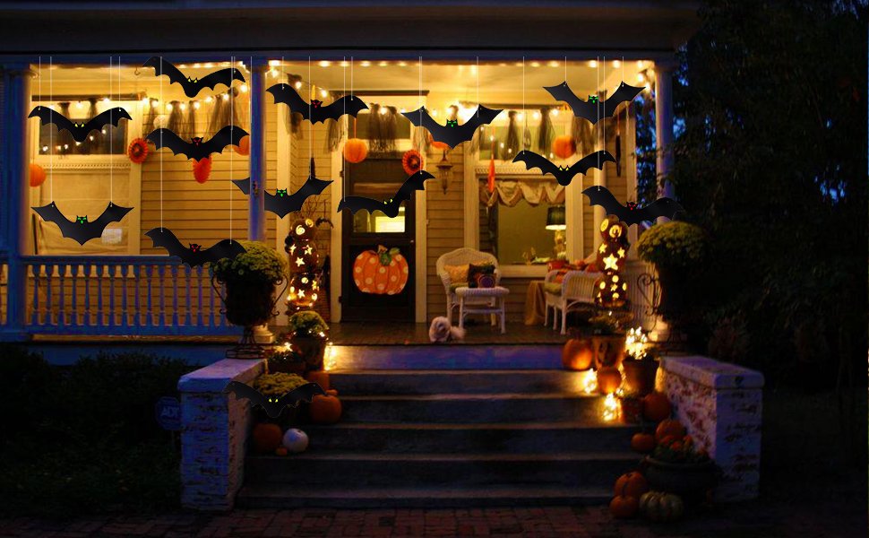 Hanging bat decorations adorn a porch at night, with glowing eyes and Halloween pumpkins.