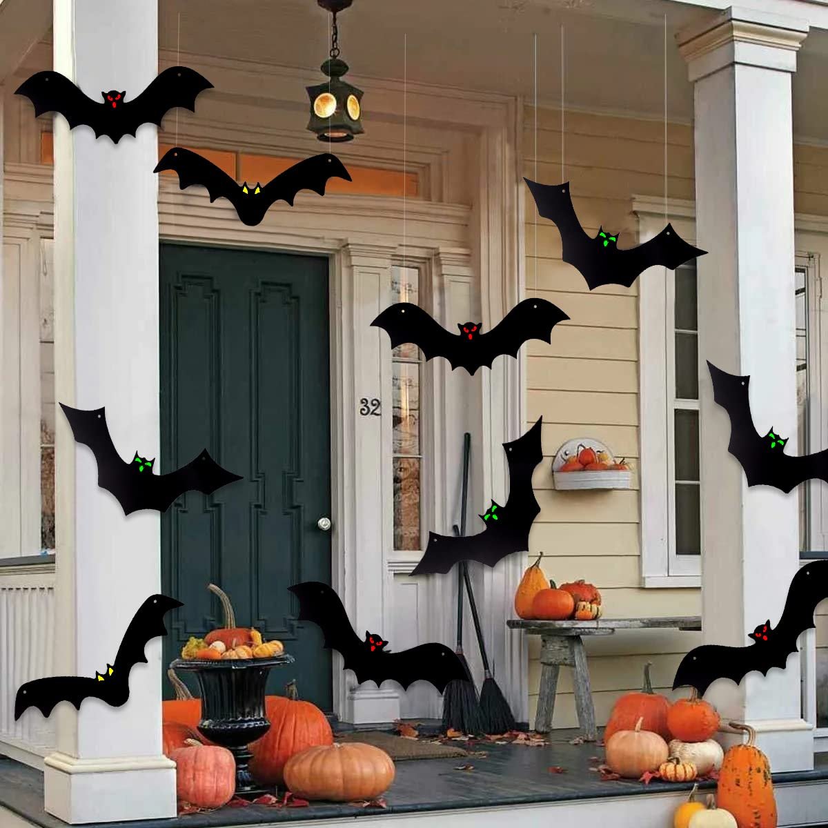 Hanging black bat decorations with glowing eyes on a porch for Halloween, surrounded by pumpkins.