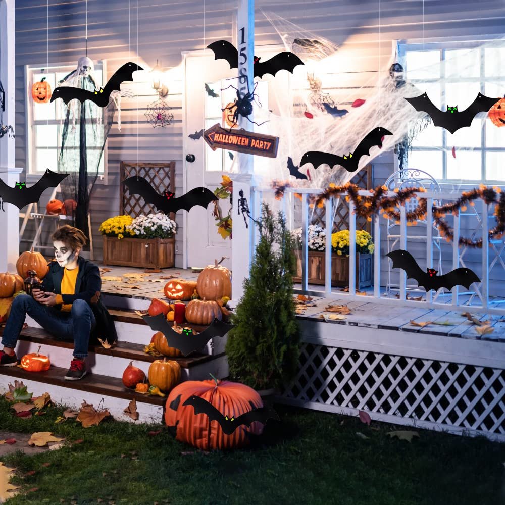 Halloween porch decorated with hanging bats, pumpkins, and a child with face paint sitting on steps.