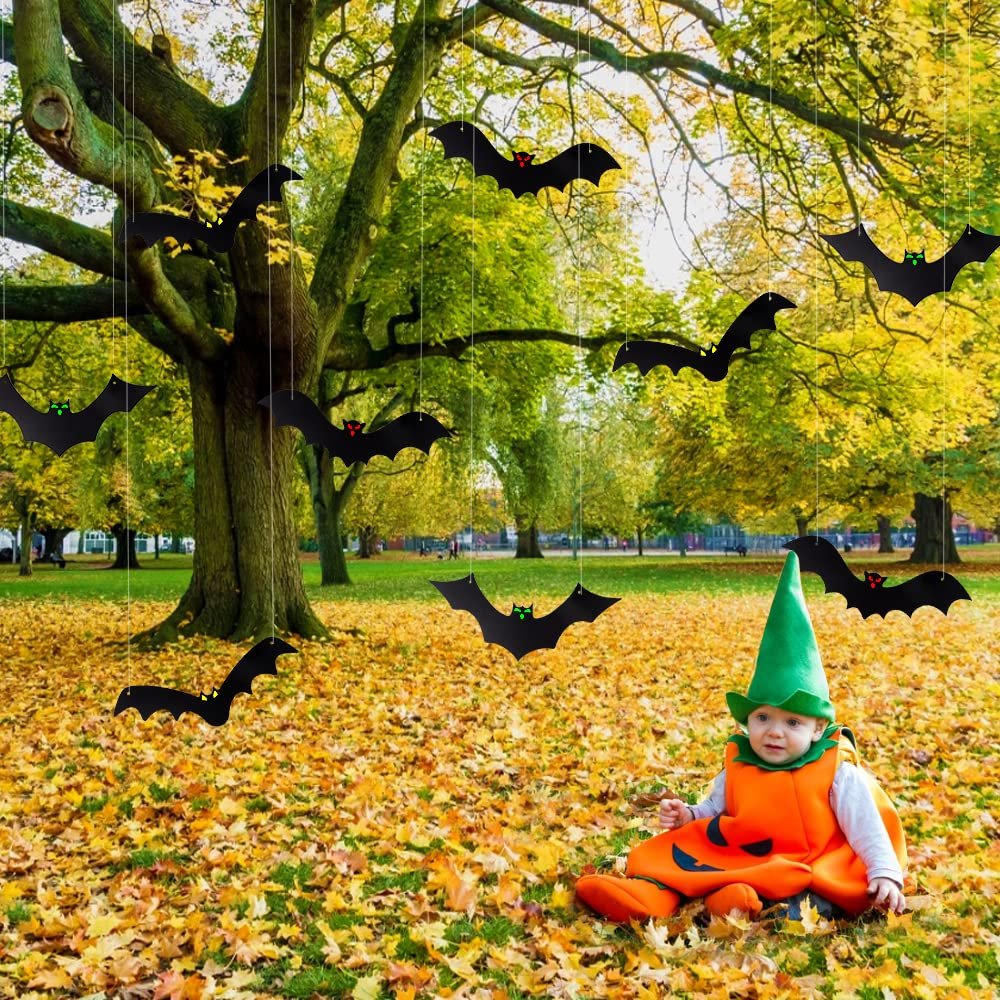 Hanging black bat decorations with glowing eyes in a park setting with a baby in a pumpkin costume