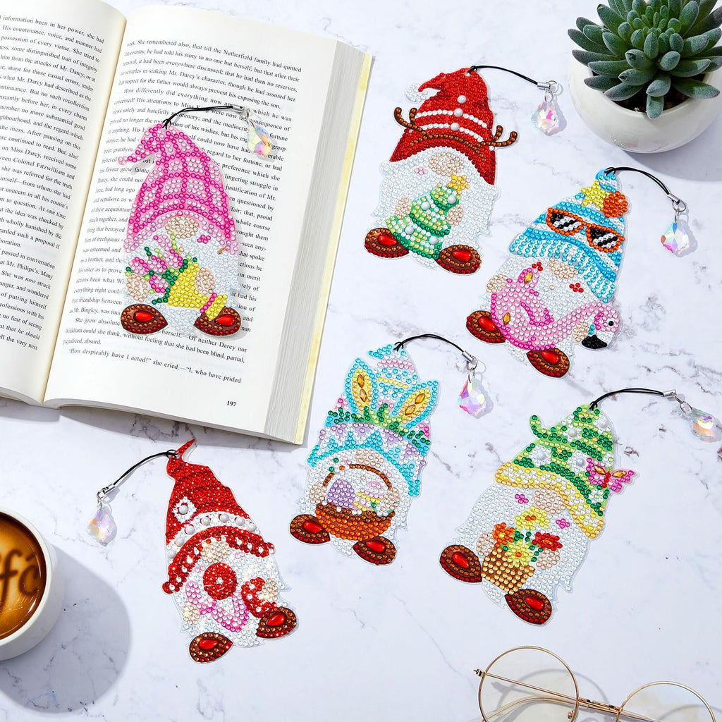 Diamond painting gnome bookmarks with crystal charms, laid out on a marble surface next to an open book.