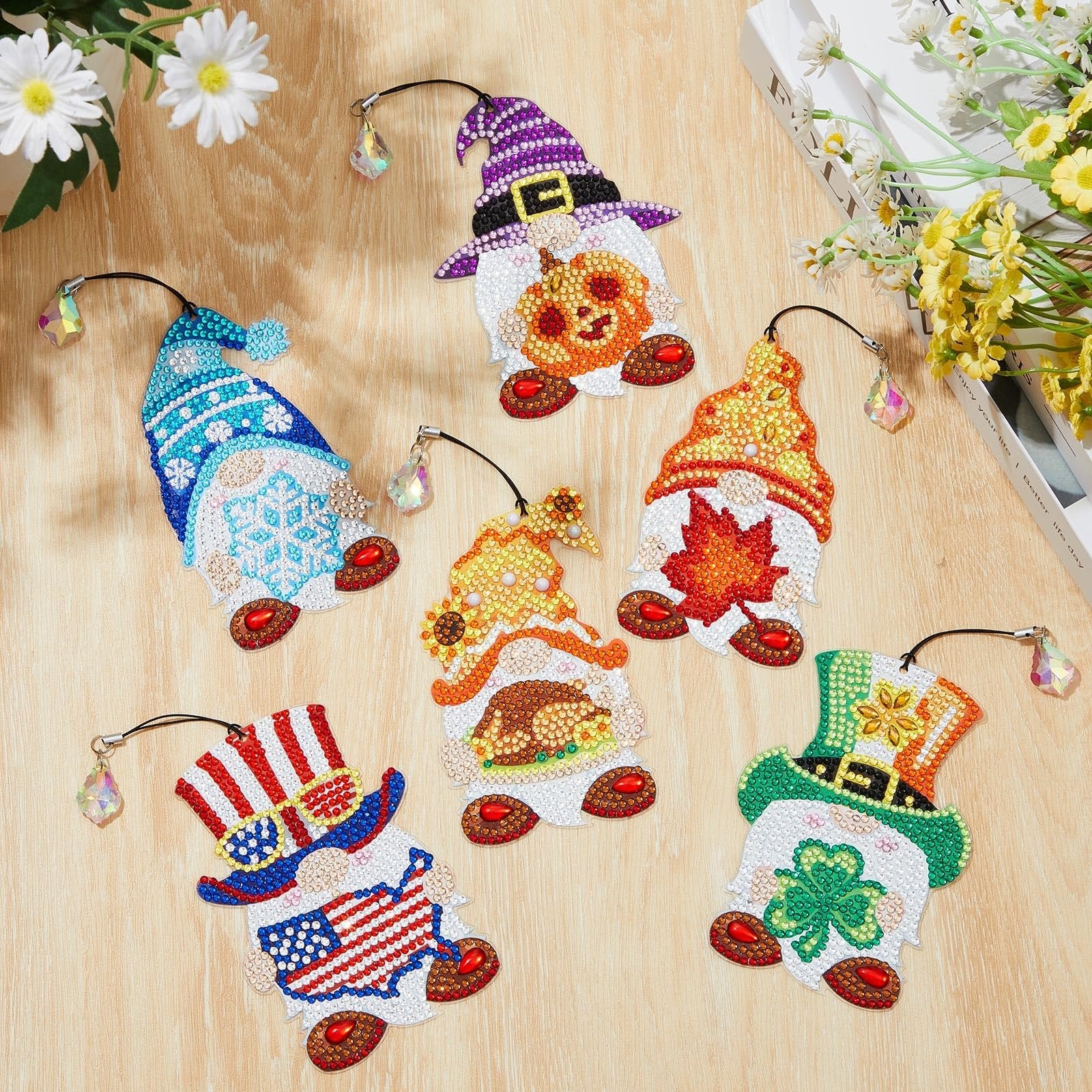 Six diamond painting gnome bookmarks with crystal charms on a wooden surface, featuring holiday themes like Halloween, Thanksgiving, and St. Patrick's Day.
