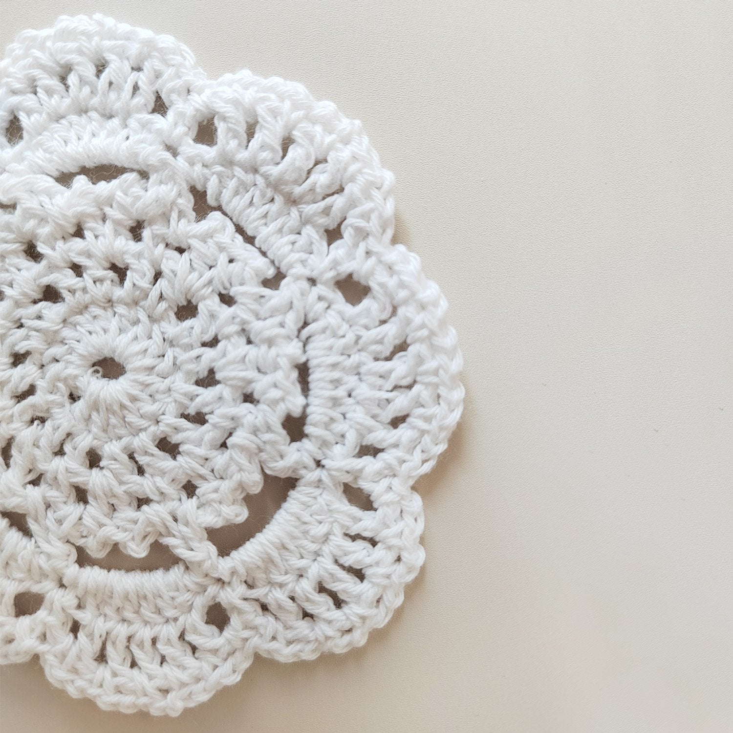 Close-up of a white handmade crochet doily with intricate floral pattern, placed on a light beige surface.