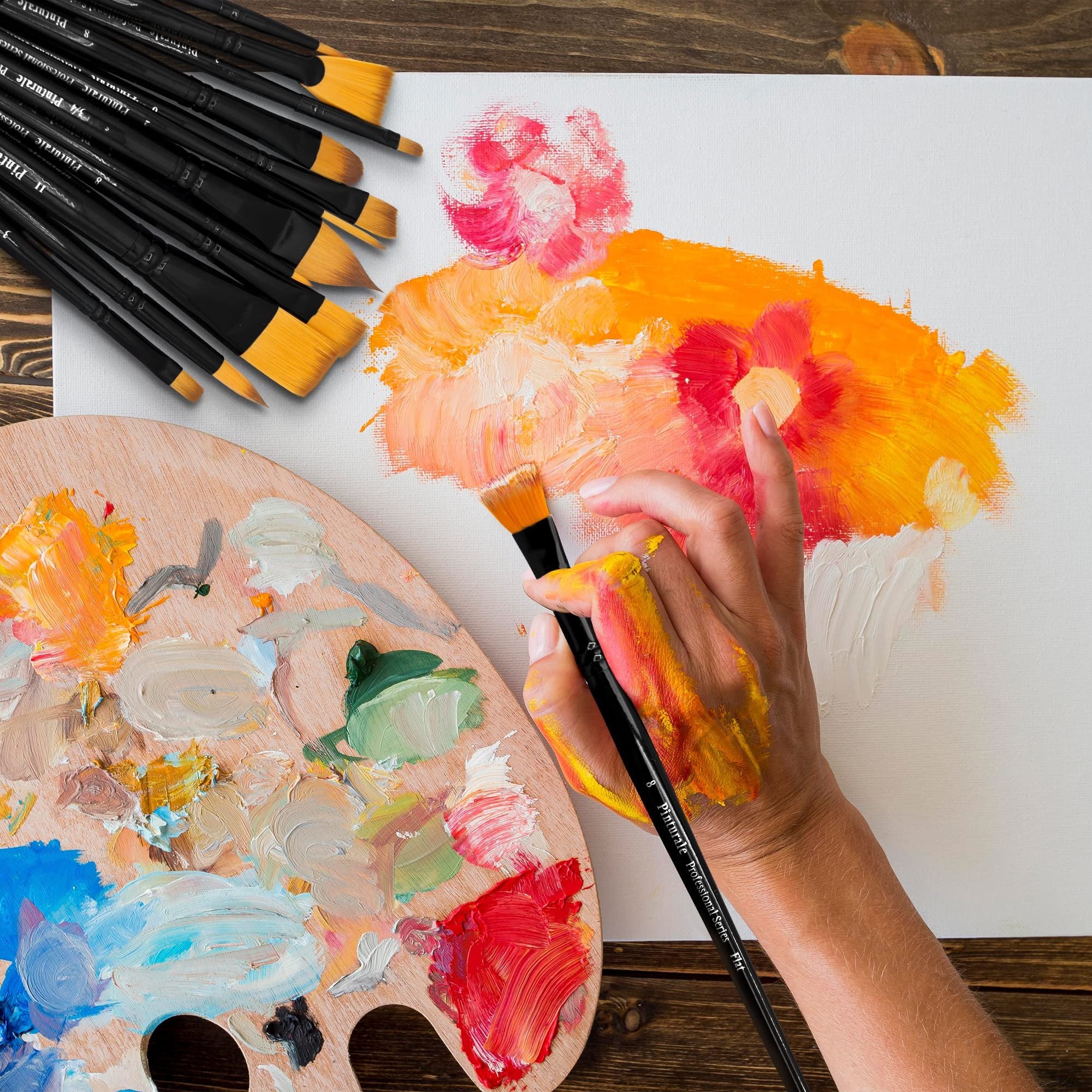 Artist's hand holding a paintbrush, applying paint to a canvas, with a palette and brush set nearby.