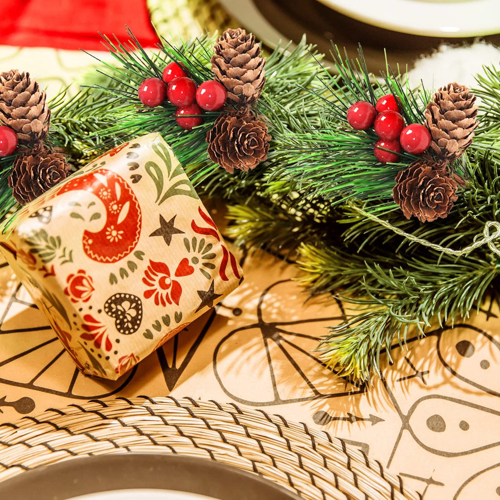 Christmas pine branch with red berries and pine cones next to a gift box with folk art pattern