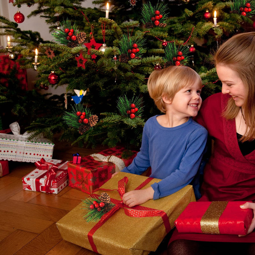 Mother and child with Christmas gifts under a decorated tree, featuring pine branches with red berries and pine cones.