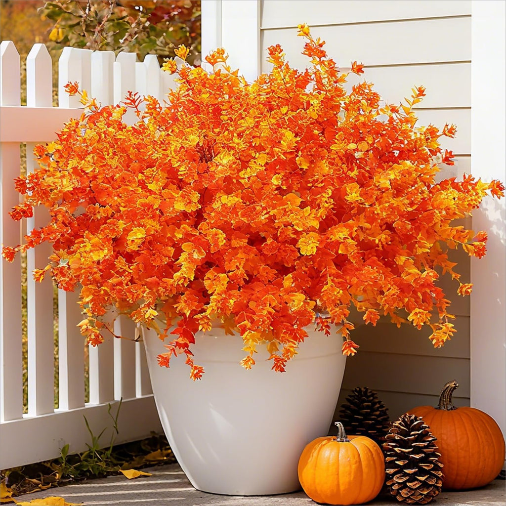 Artificial orange fall bushes in a white pot with pumpkins and pinecones on a porch