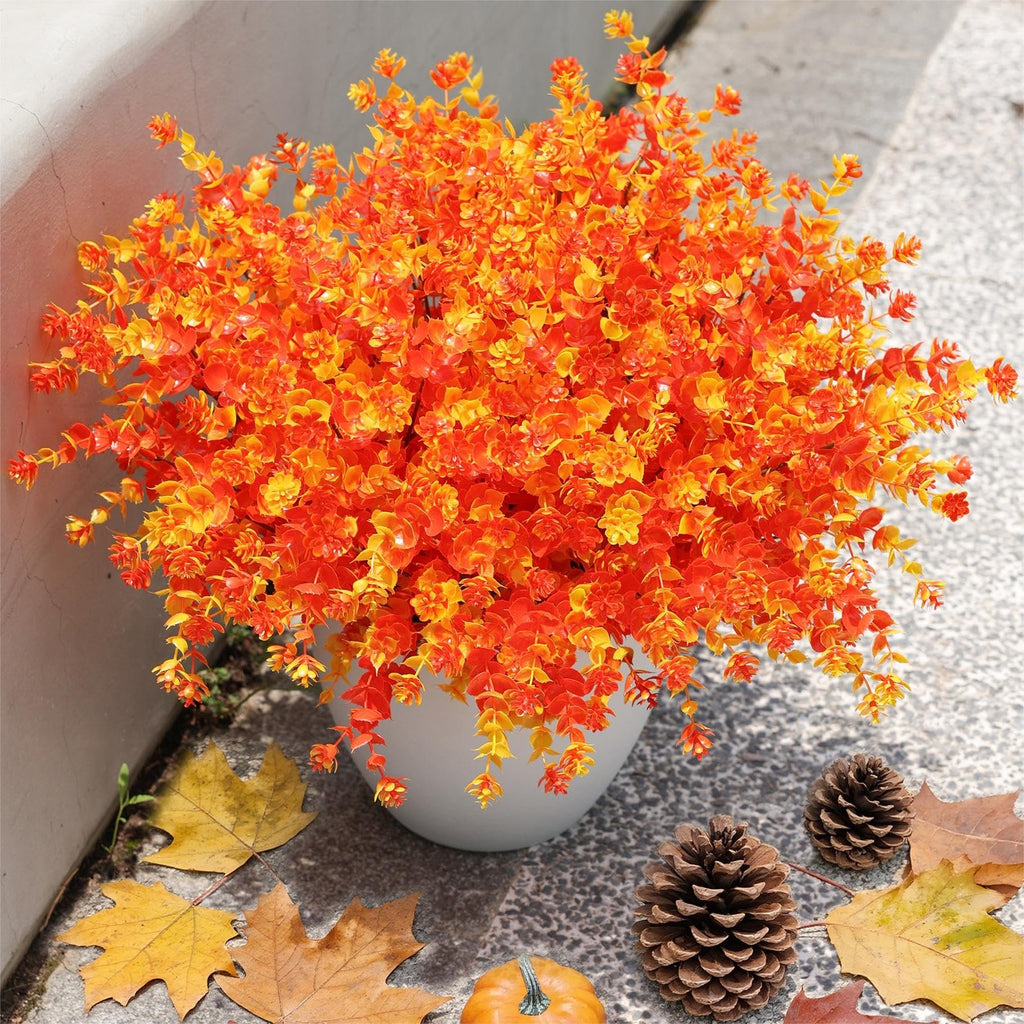 Artificial orange and yellow fall bushes in a white pot with pinecones and autumn leaves on the ground