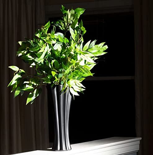 Artificial Italian ruscus greenery stems in a black vase on a windowsill with curtains.