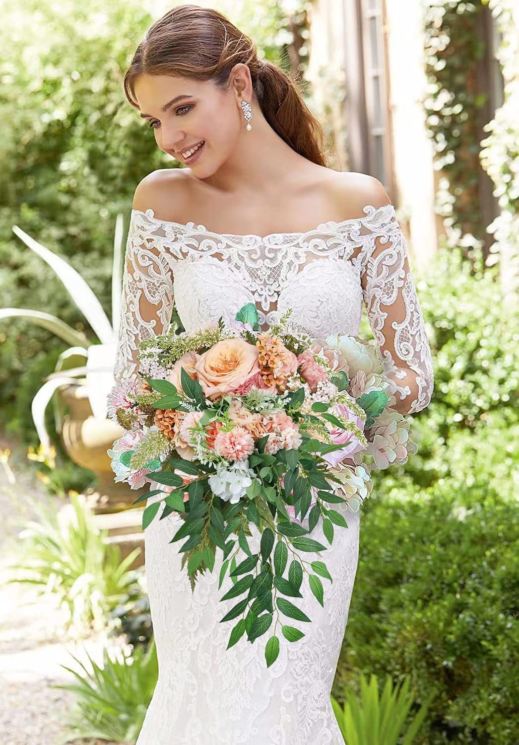 Bride in a white lace dress holding a cascading bouquet of artificial flowers and greenery