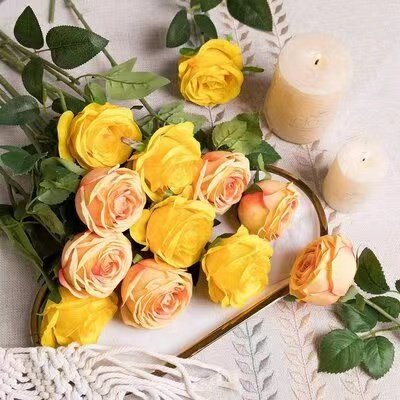 A dozen yellow and peach silk roses arranged with two lit candles on a decorative tray.