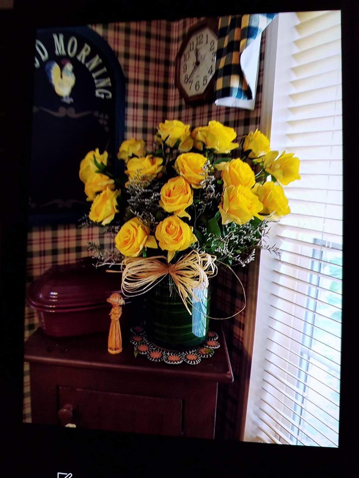Bouquet of yellow silk roses in a green vase with a raffia bow, on a wooden table with decor.