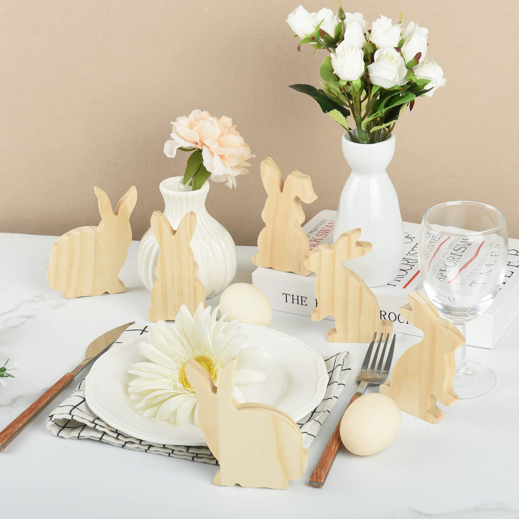 Unfinished wooden Easter bunny cutouts arranged on a table with decorative eggs and flowers.