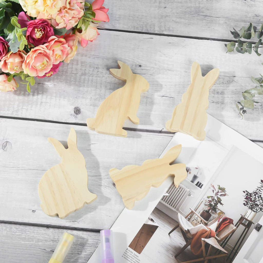 Four unfinished wooden bunny cutouts arranged on a light wooden surface with decorative flowers and eucalyptus branches.