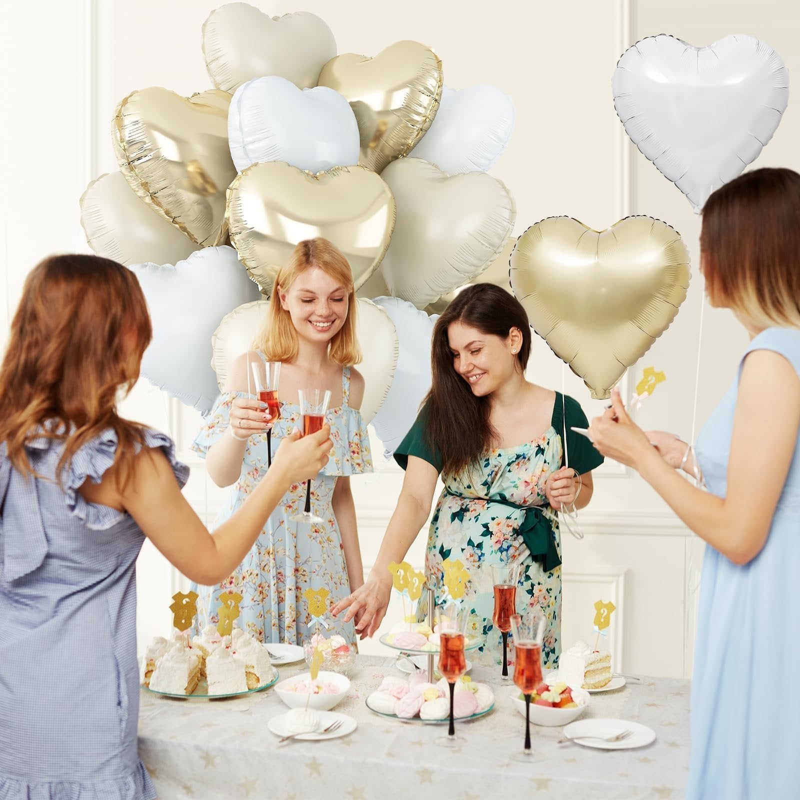 Four women celebrating with heart-shaped balloons and desserts at a party table.