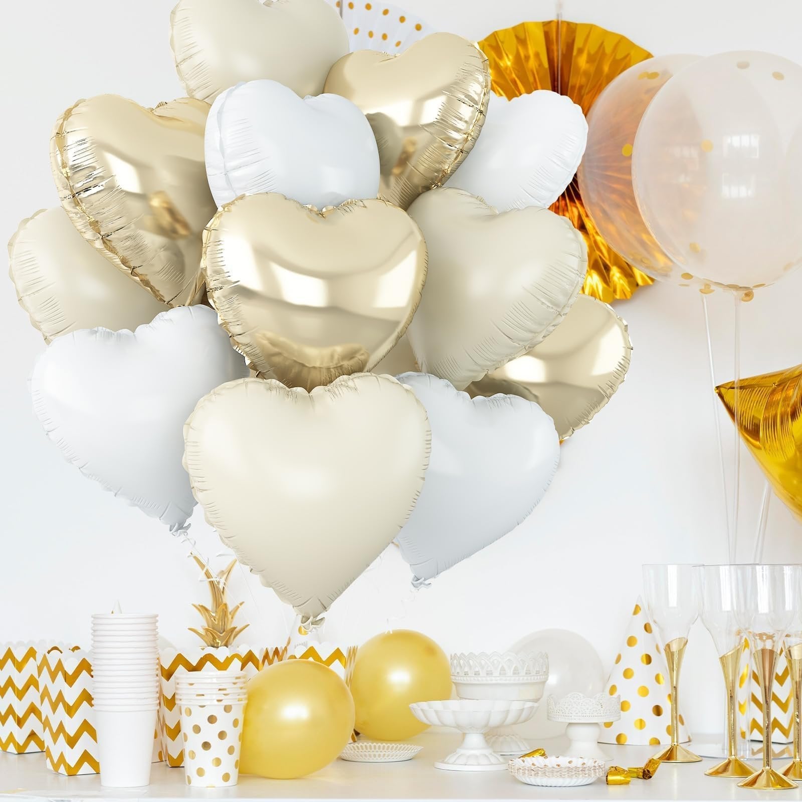 A bouquet of cream white, white, and light gold heart-shaped foil balloons arranged on a white surface with party decorations.