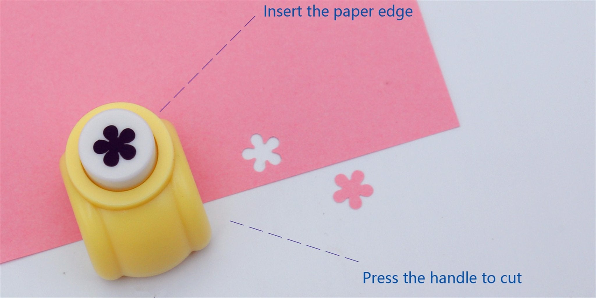 Yellow flower-shaped craft puncher creating cutouts in pink paper on a white surface