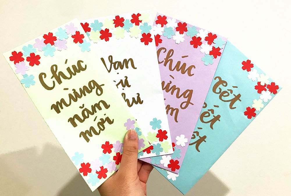 Hand holding four decorative envelopes with floral borders and gold calligraphy