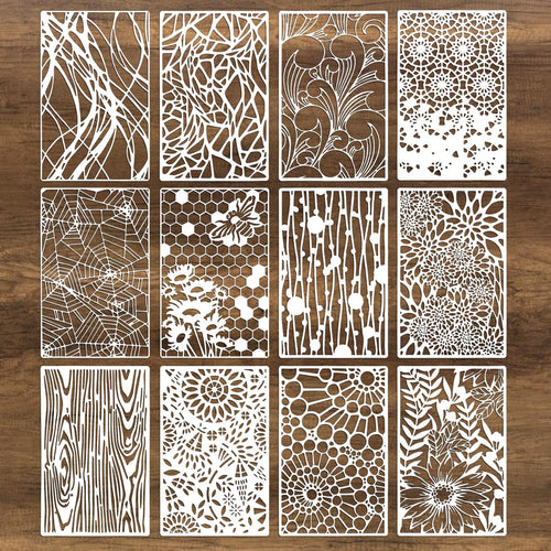 Twelve white stencils with intricate cut-out designs including spider webs, flowers, wood grain, and geometric patterns, arranged in a 3x4 grid on a brown wooden background.