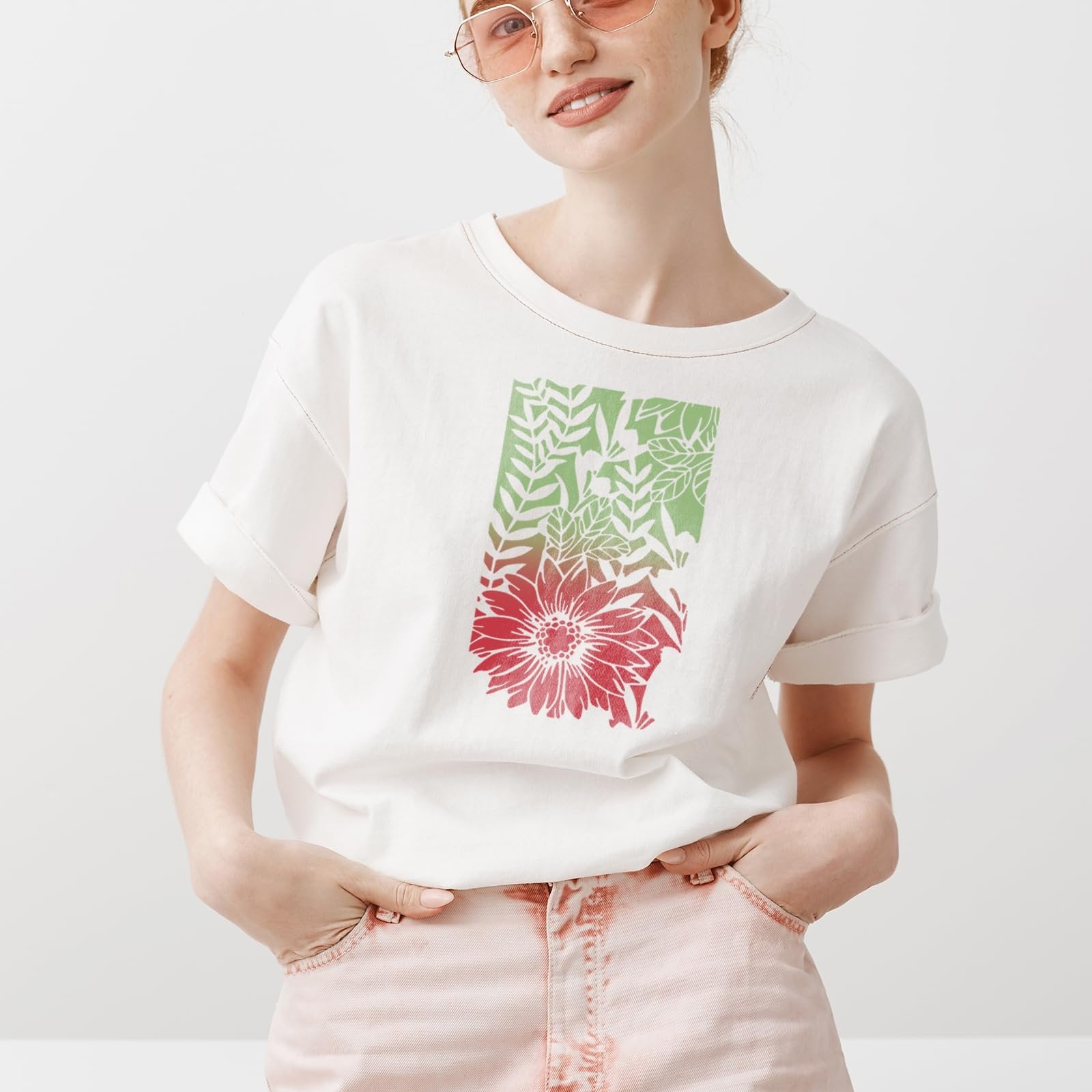Woman wearing a white t-shirt with a floral and leaf stencil design in red and green.