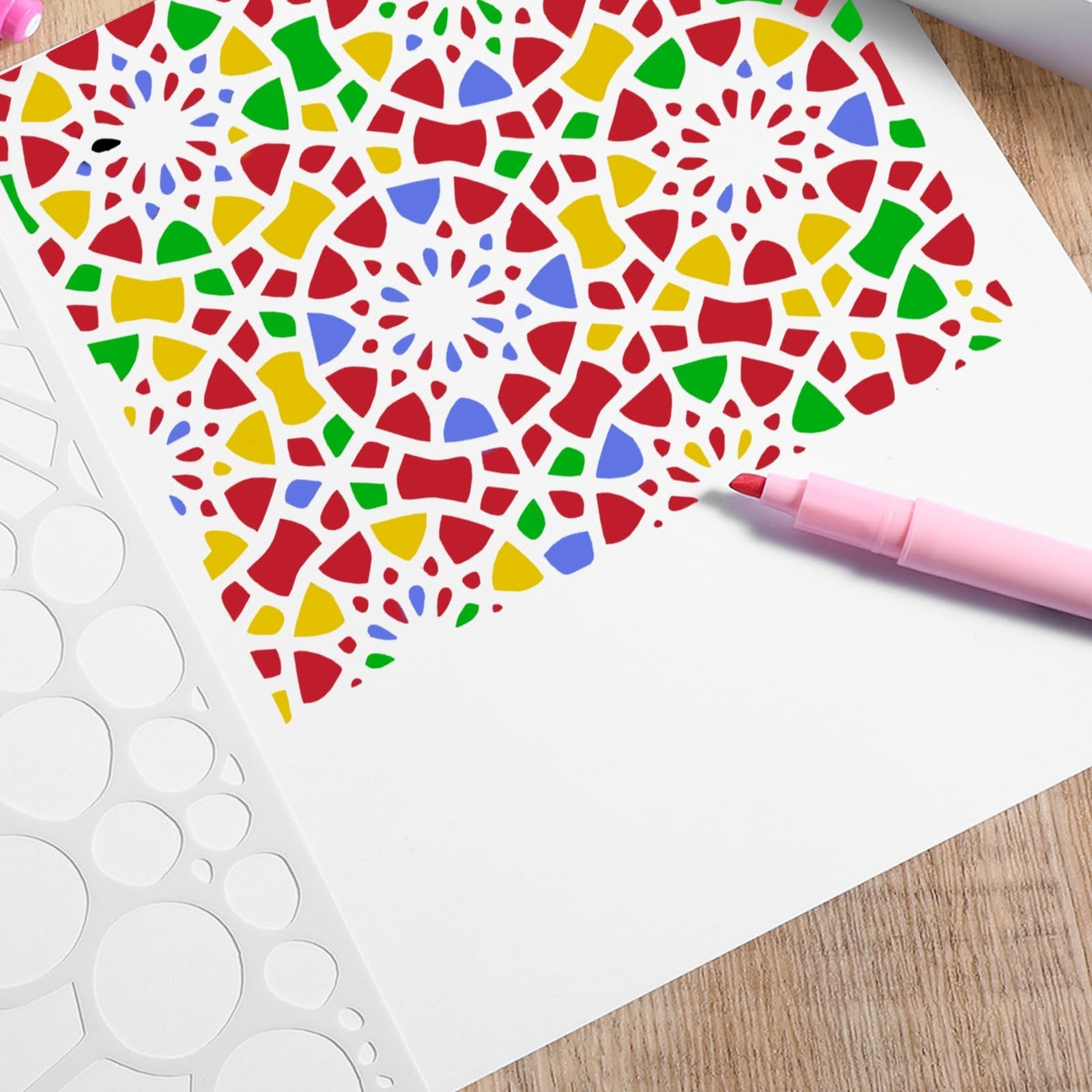 Painting stencil with colorful geometric pattern being applied to white paper with a pink marker