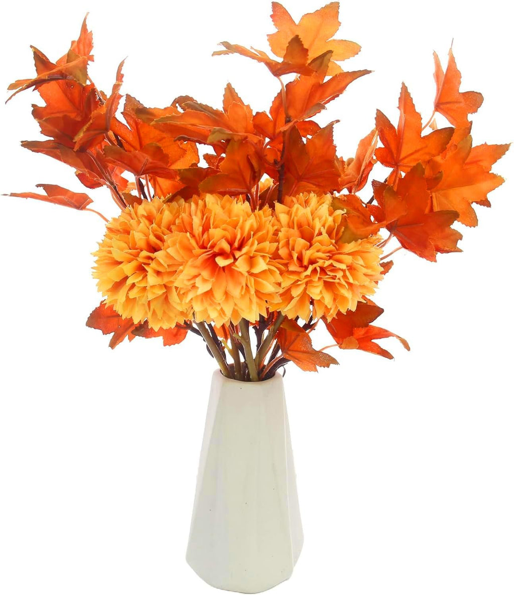 Orange artificial chrysanthemum flowers and maple leaves in a white vase, close-up view