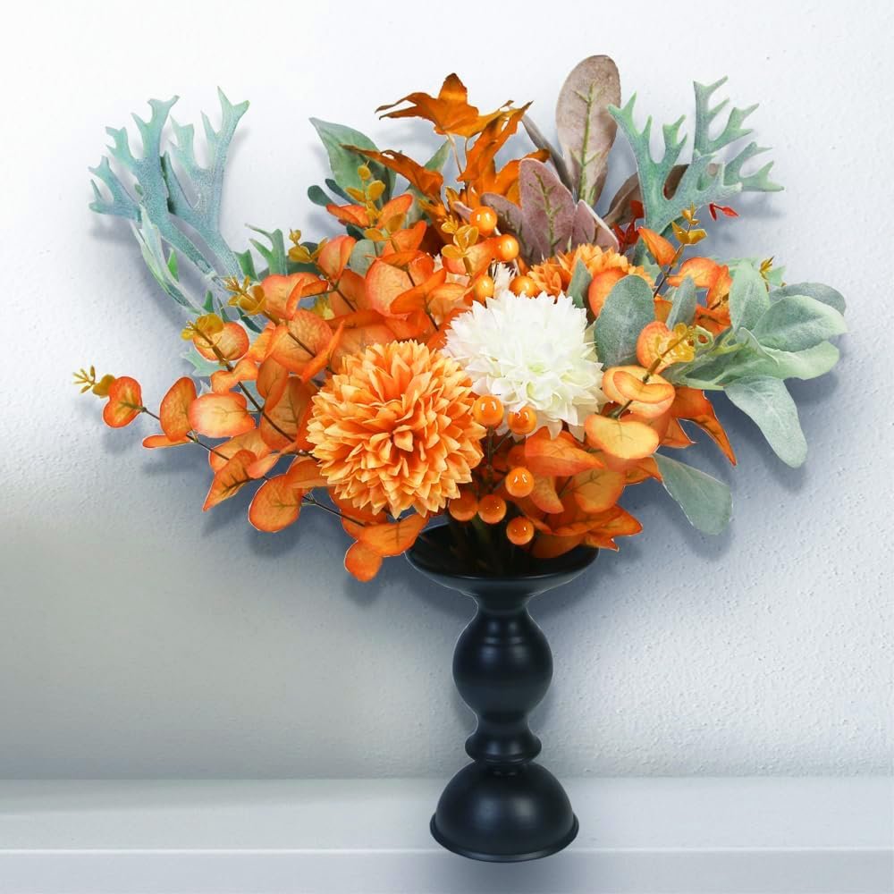 Artificial orange chrysanthemum flowers and eucalyptus in a black vase, arranged for fall decor.