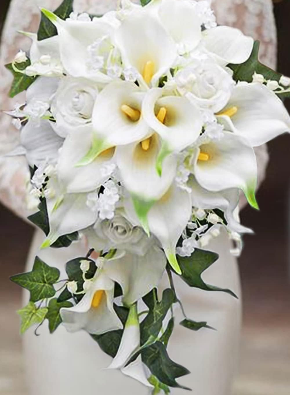 White calla lily and rose bridal bouquet with green ivy accents, held by a person in a lace dress.