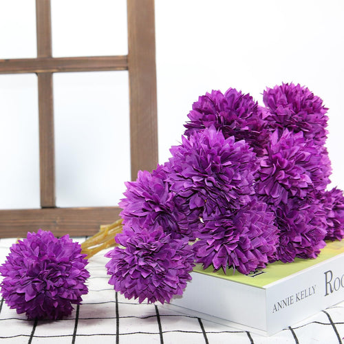 Bouquet of purple artificial chrysanthemum flowers resting on a book with text, against a wooden window frame backdrop.