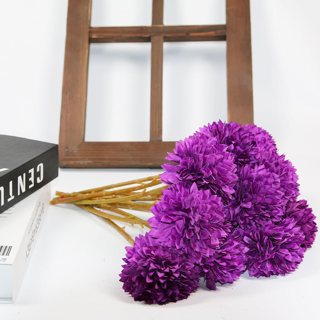 Bouquet of purple artificial chrysanthemum flowers with stems, lying next to a book and a wooden frame.