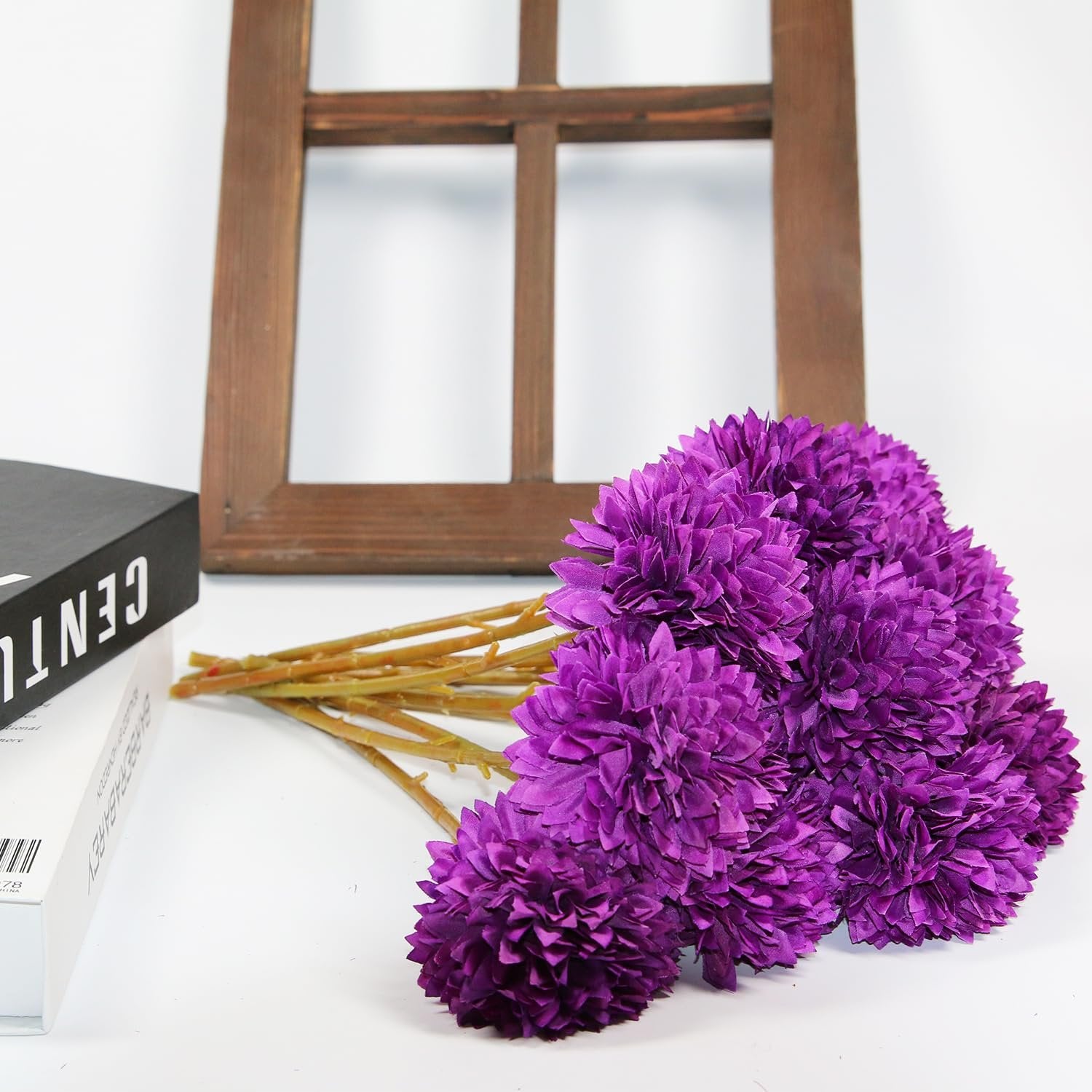 Bouquet of purple artificial chrysanthemum flowers with stems, lying next to a book and a wooden frame.