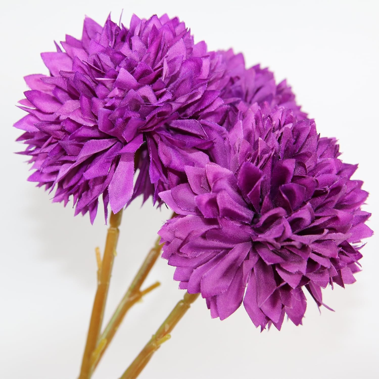 Three purple artificial chrysanthemum flowers with fabric petals and brown stems against a white background.