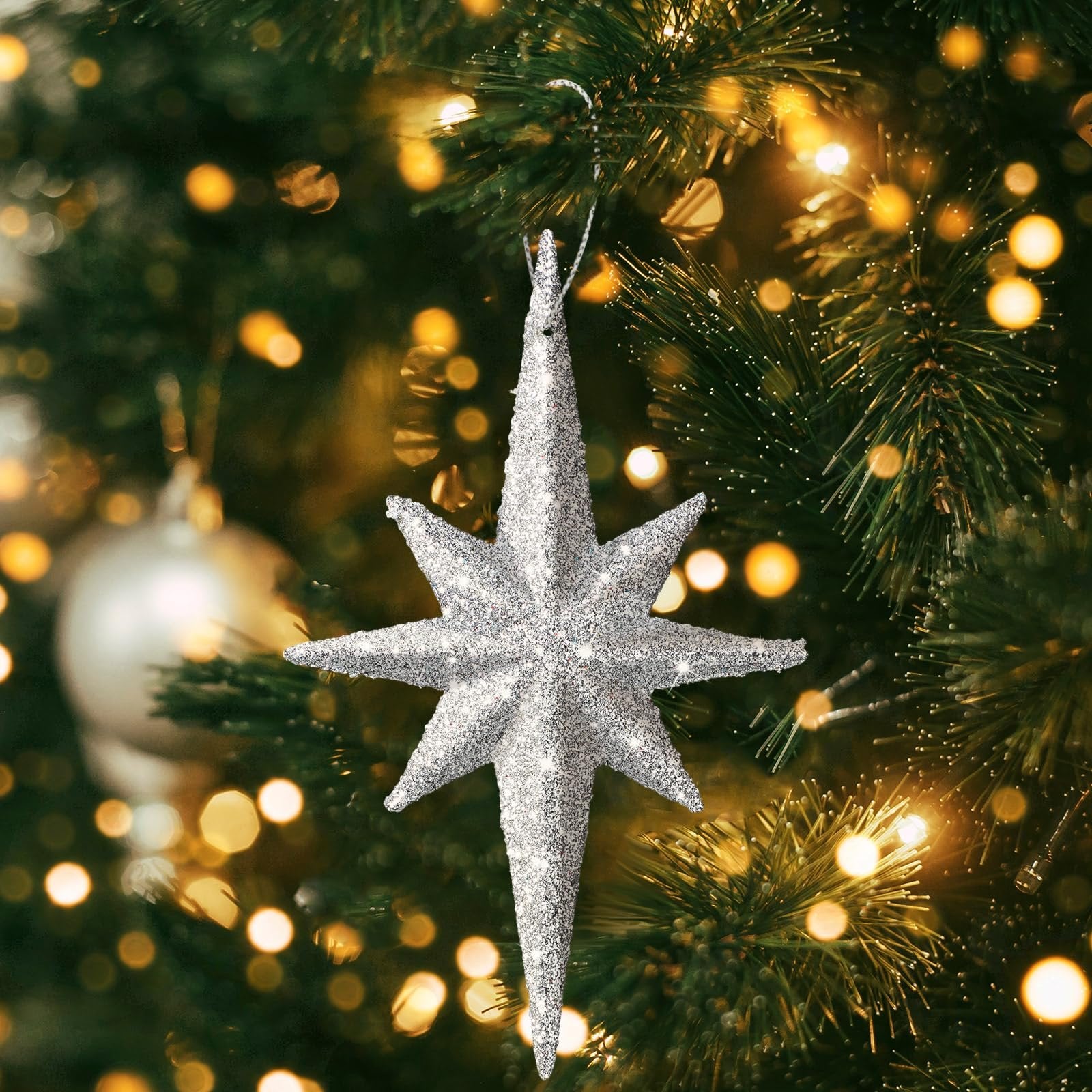 Silver glitter Bethlehem star ornament hanging on a Christmas tree with bokeh lights