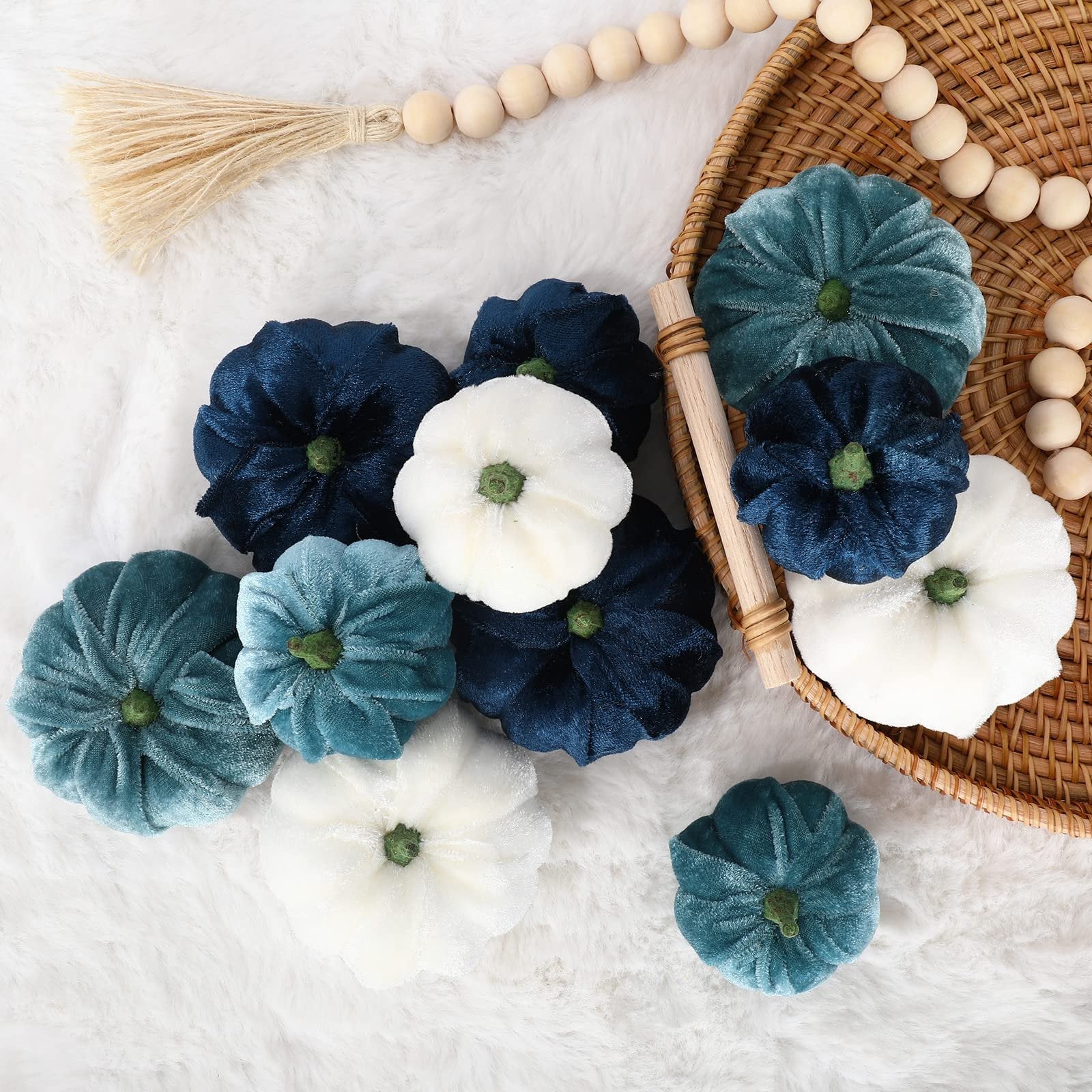 Velvet artificial pumpkins in blue, white, and teal arranged on a fluffy white surface and in a woven basket.
