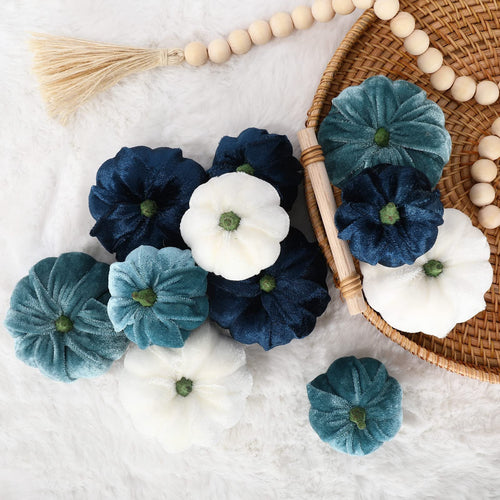 Velvet artificial pumpkins in blue, white, and teal arranged on a fluffy white surface and in a woven basket.