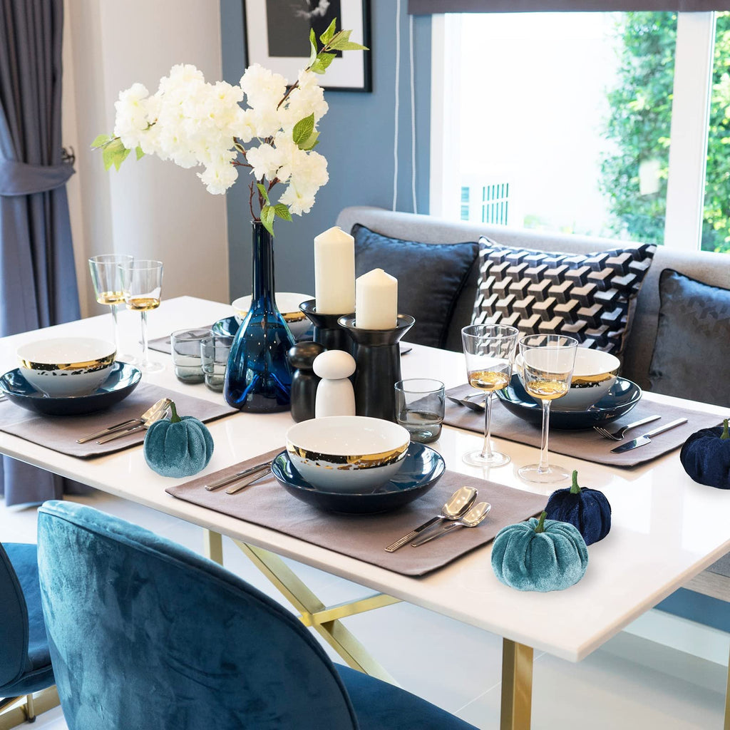 Velvet artificial pumpkins in blue and navy set on a dining table with place settings and floral arrangement.