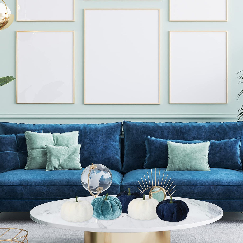 Velvet pumpkins in blue and white arranged on a marble coffee table in front of a blue sofa.