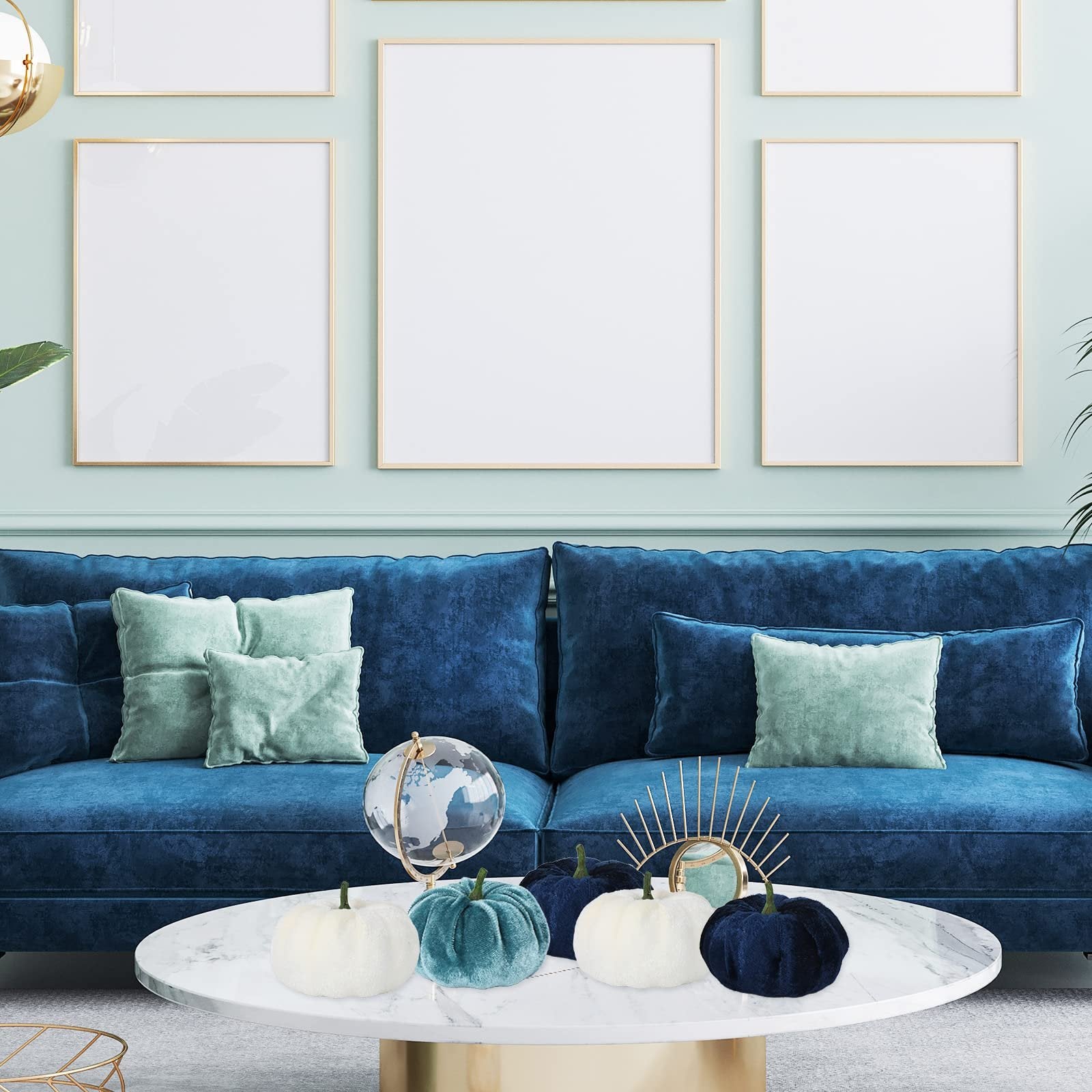 Velvet pumpkins in blue and white arranged on a marble coffee table in front of a blue sofa.