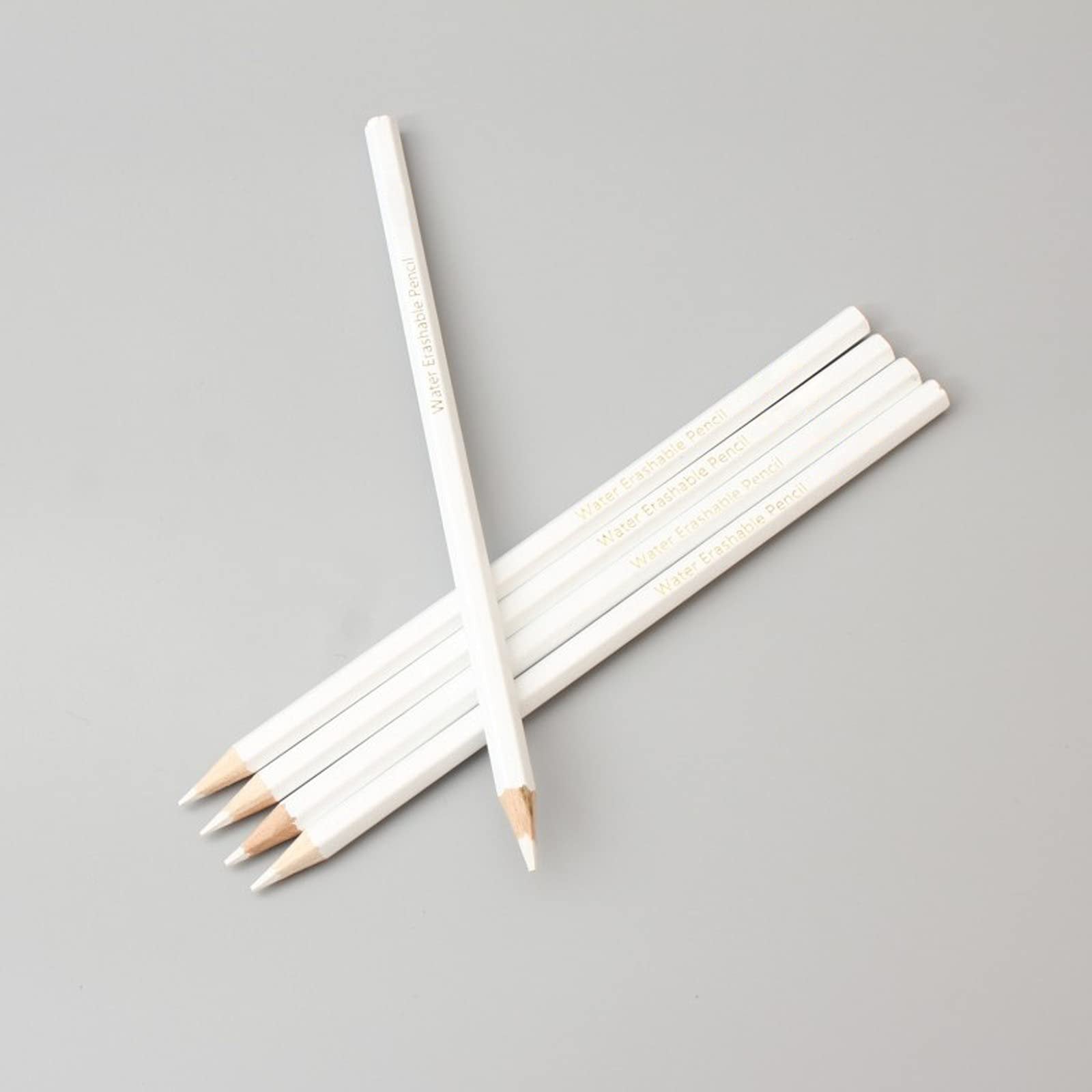 Several white water-soluble marking pencils arranged diagonally on a gray background, with text printed on their sides.