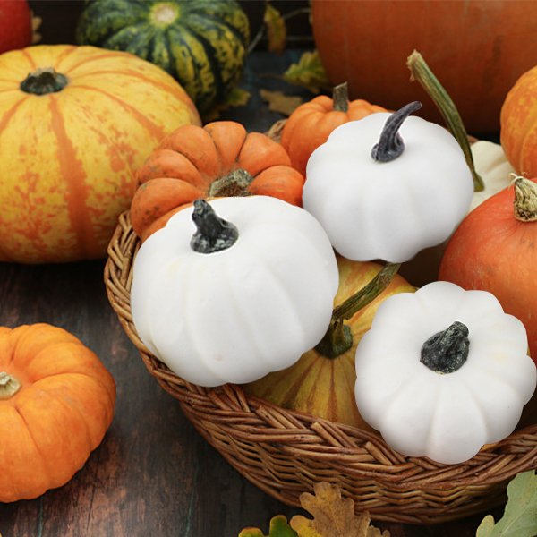 Assorted white and orange pumpkins in a woven basket with fall leaves on a wooden surface