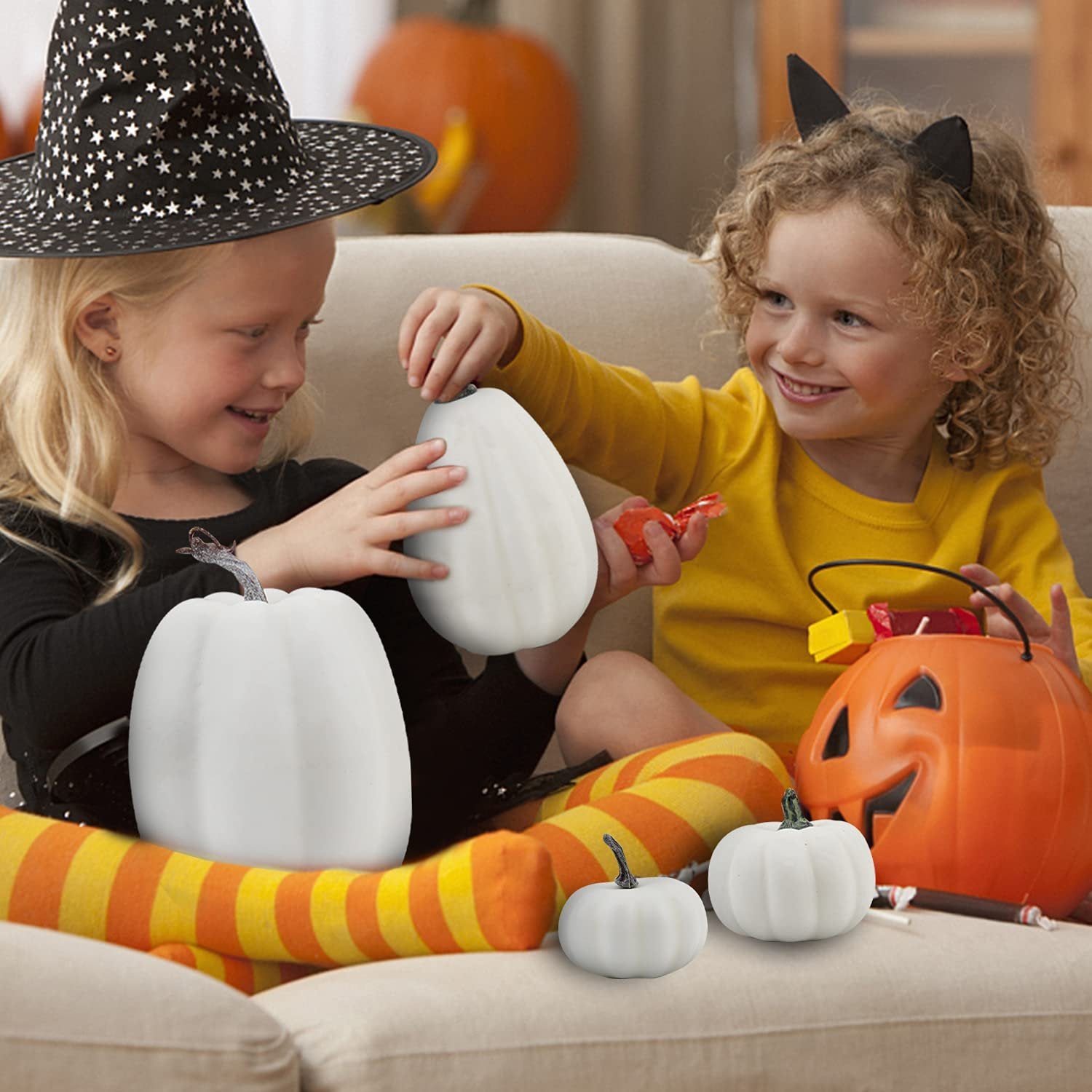 Two children in Halloween costumes playing with white foam pumpkins on a couch.