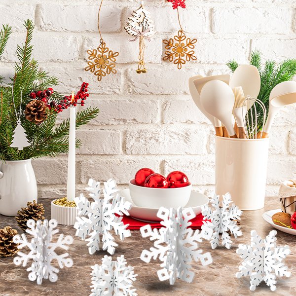 White wooden 3D snowflake decorations arranged on a countertop with Christmas tree branches, pinecones, and red ornaments.