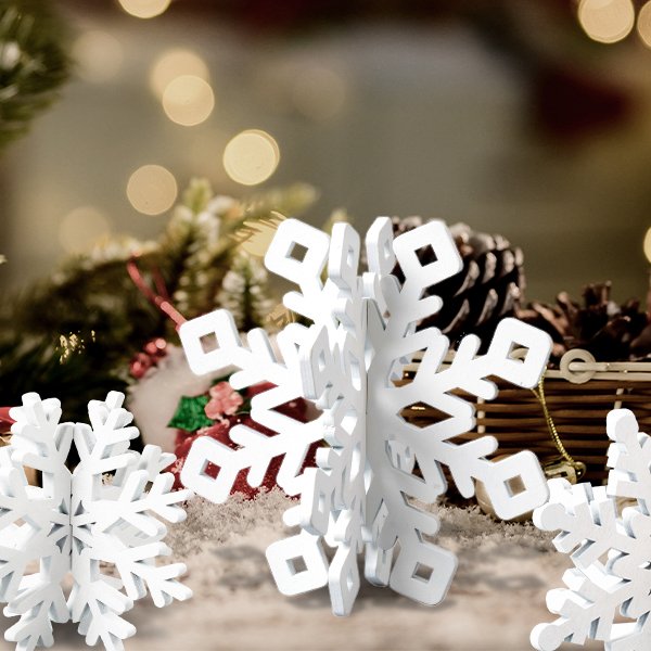 Three white wooden 3D snowflake decorations on a festive background with pinecones and greenery