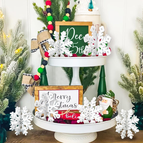 Tiered tray decorated with white wooden snowflakes, festive signs, and Christmas figurines.