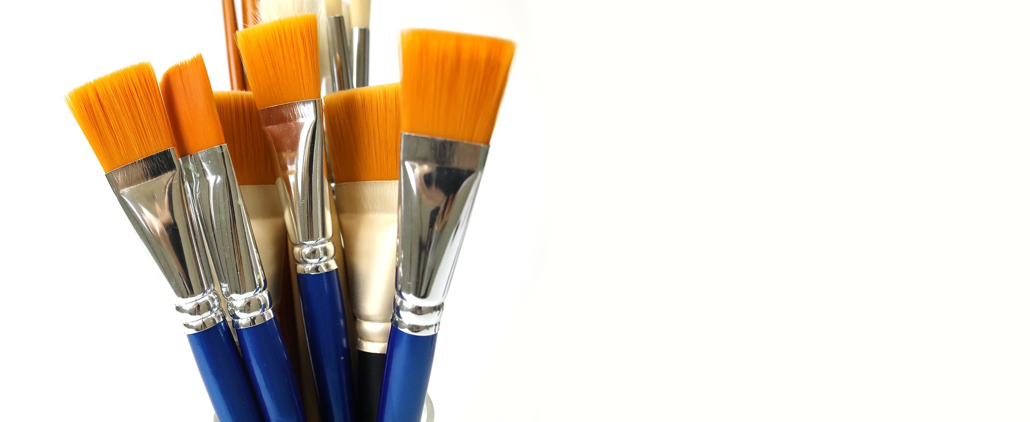 Close-up of a collection of flat paint brushes with orange synthetic bristles and silver ferrules, some with blue wooden handles, against a white background.